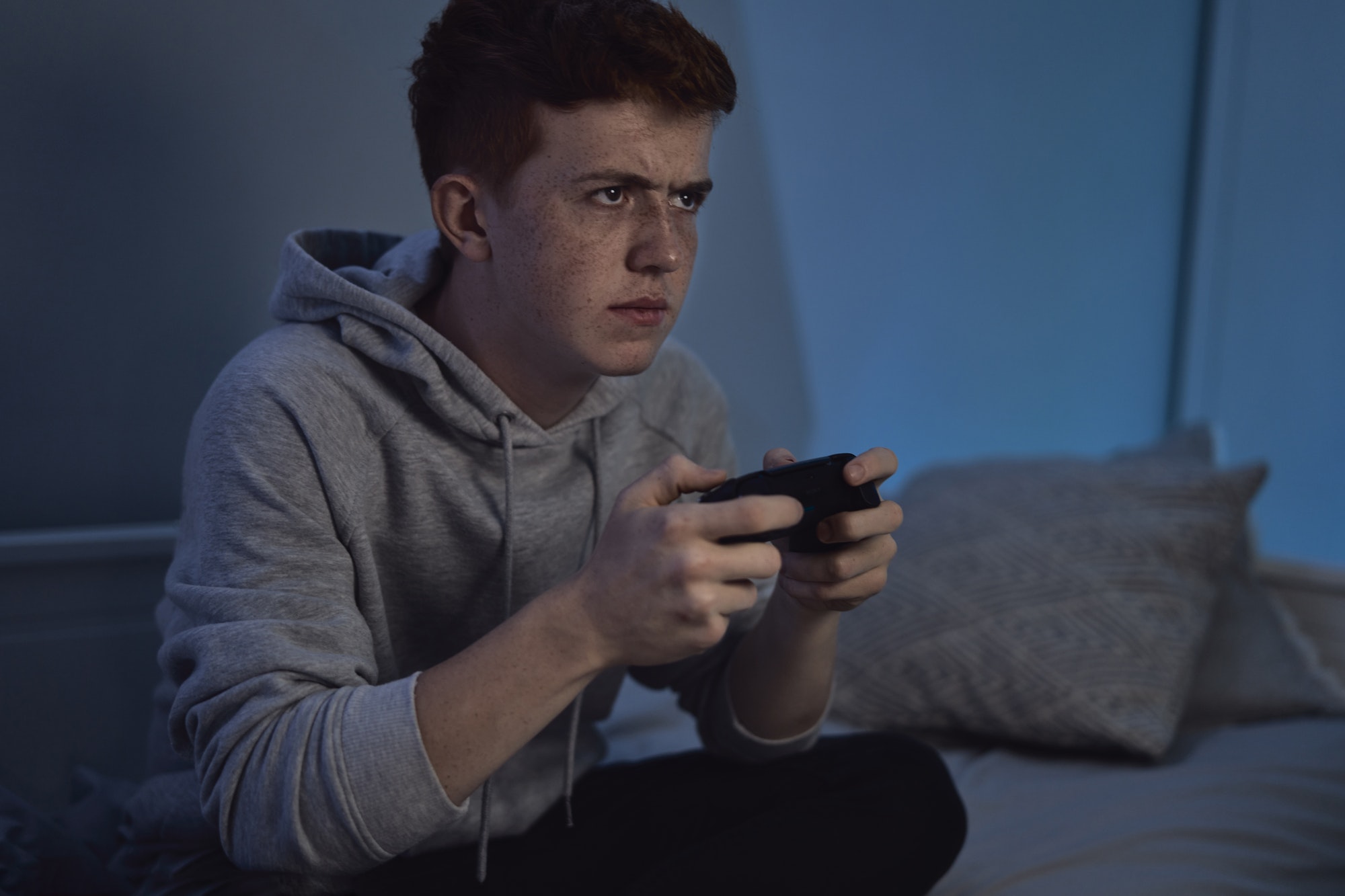 Caucasian teenage boy playing on game controller at night